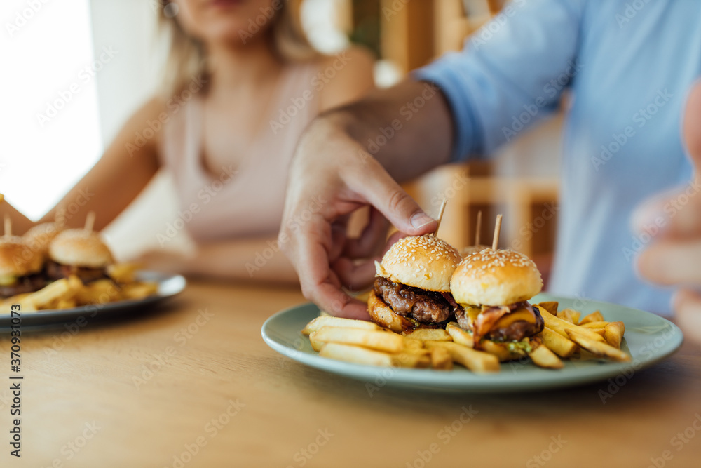 Eating mini burgers with friends, close-up. Eating mini burgers with friends, close-up.