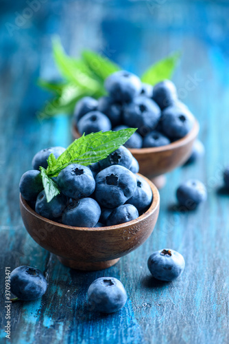 Foto Bowl of fresh blueberries on blue rustic wooden table closeup.