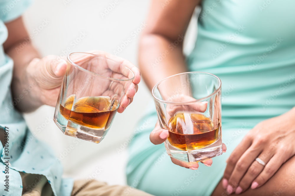 Man and woman hands toasting with glasses of whiskey brandy or rum indoors - closeup Man and woman hands toasting with glasses of whiskey brandy or rum indoors - closeup