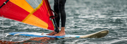 Man in a wetsuit standing on a windsurfing board