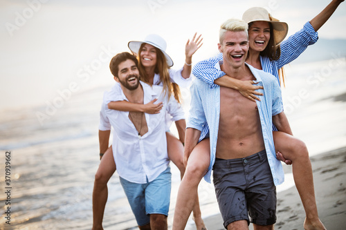 Group of happy friends having fun walking down the beach at sunset