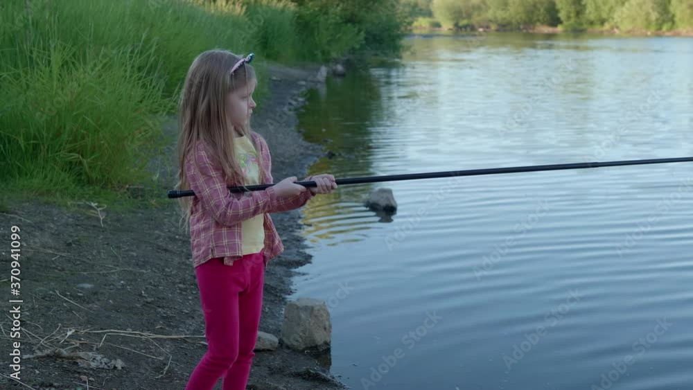 Vew from the side of little girl with fishing rod catches fish by the river in the summer. Vew from the side of little girl with fishing rod catches fish by the river in the summer.