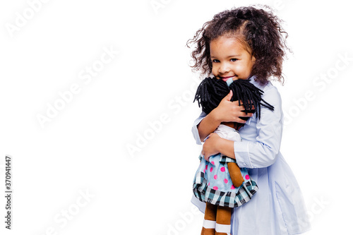 Photographie Portrait of a cute little african american girl hugging doll, isolated on white background