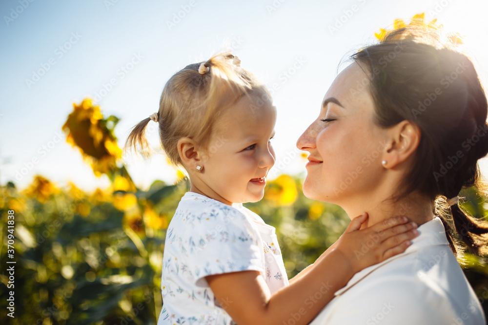 Happy mother with the daughter in the field with sunflowers having fun on a sunny summer day. Family value, unity, happiness, love and joy concept. Happy mother with the daughter in the field with sunflowers having fun on a sunny summer day. Family value, unity, happiness, love and joy concept.