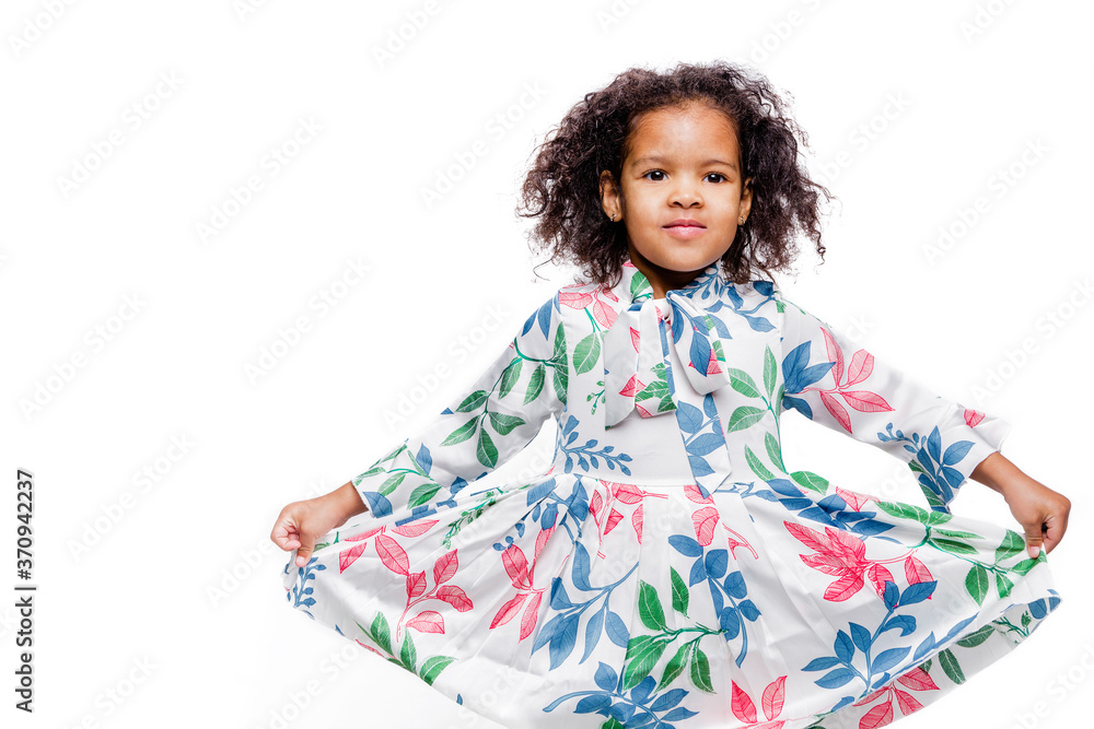 Little cute fashionable African American girl wearing white floral dress. The girl stretches the dress wide and shows how beautiful it is Little cute fashionable African American girl wearing white floral dress. The girl stretches the dress wide and shows how beautiful it is