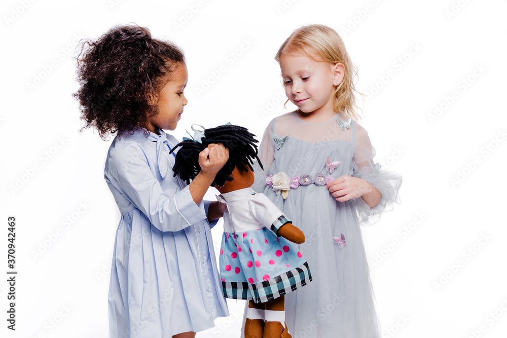 Little fashionable girls are friends of two different nationalities. African American girl showing doll to her friend Little fashionable girls are friends of two different nationalities. African American girl showing doll to her friend
