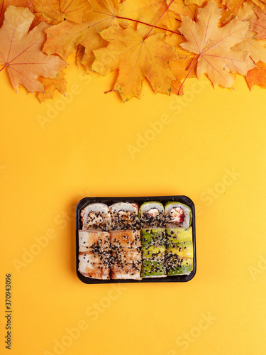 set of sushi rolls on a yellow background. autumn composition with yellow leaves. autumn mood