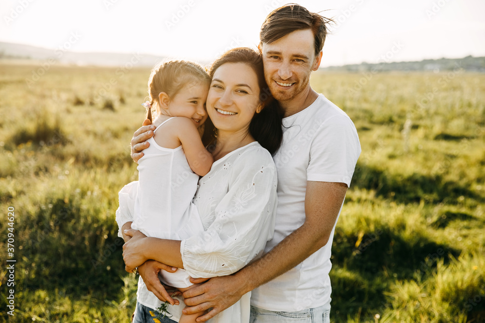 Family mother, father and daughter in an open field, hugging and smiling. Family mother, father and daughter in an open field, hugging and smiling.