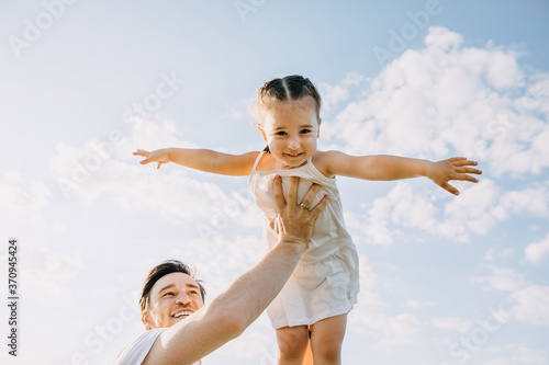 Father and daughter playing outdoors on a summer day. Man holding little girl up in the sky.