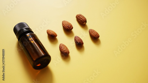 Bottle of almond oil and almonds on yellow background - Bottle and rows of nuts
