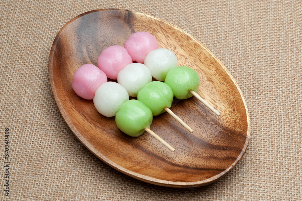 Japanese traditional sweet called Dango Mochi on wooden platter with green tea. Isolated on jute background. Close-up. Top view. Japanese traditional sweet called Dango Mochi on wooden platter with green tea. Isolated on jute background. Close-up. Top view.