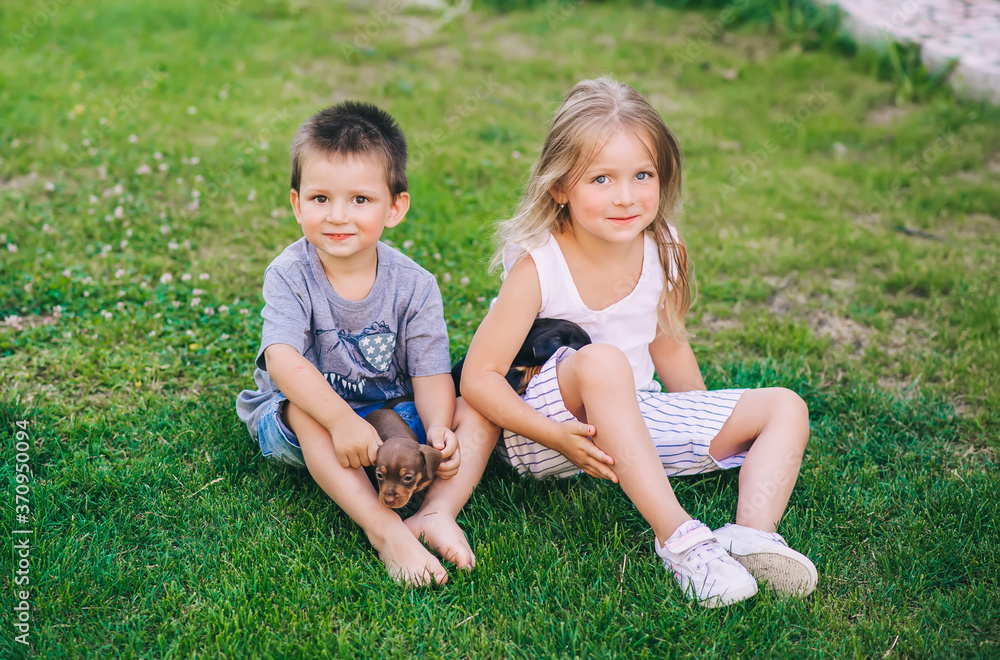 Brother and sister sitting on the grass with two puppies dachshund Brother and sister sitting on the grass with two puppies dachshund