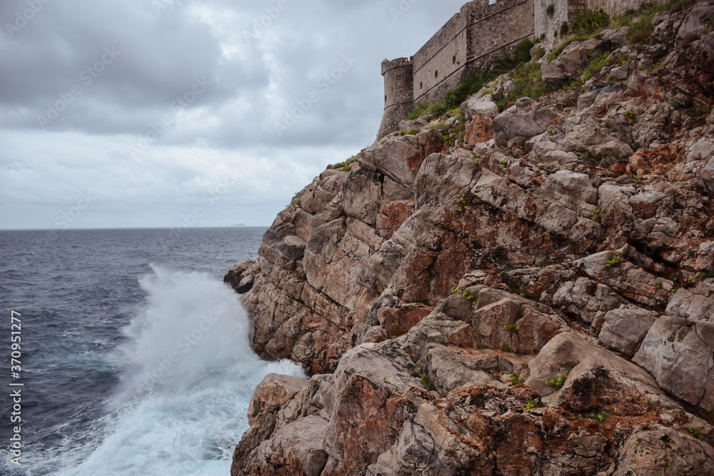wave crashing against the rocks with Dubrovnik's walls in the background