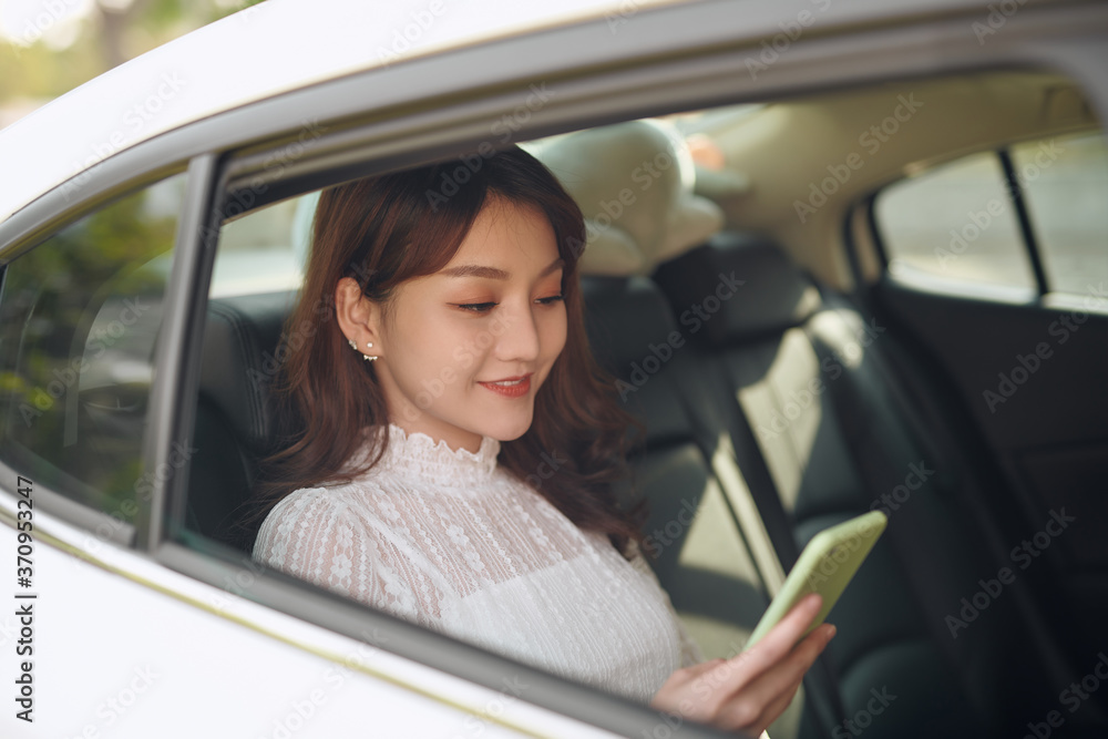Reading information from smartphone. Smart businesswoman sits at backseat of the luxury car with black interior.