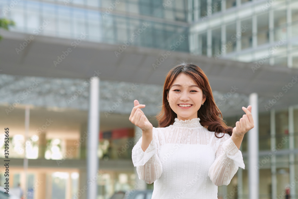 Beautiful asian woman showing mini heart sign hands on city background. Like, Love and Valentine Concept.