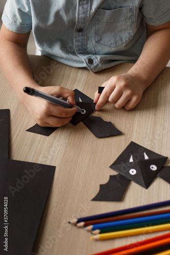 A cute little boy made a Halloween bat out of black paper. Children's handwork.