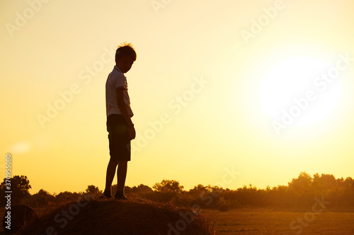 Silhouette of a child-boy standing on a haystack against the background of a field with a beautiful sunset.The concept of a carefree childhood. Beautiful summer landscape, copyspace.