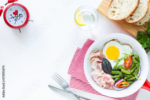 Breakfast for your beloved for the holiday: heart-shaped egg, bacon, green beans on a white table. Selective focus. View from above. Copy space