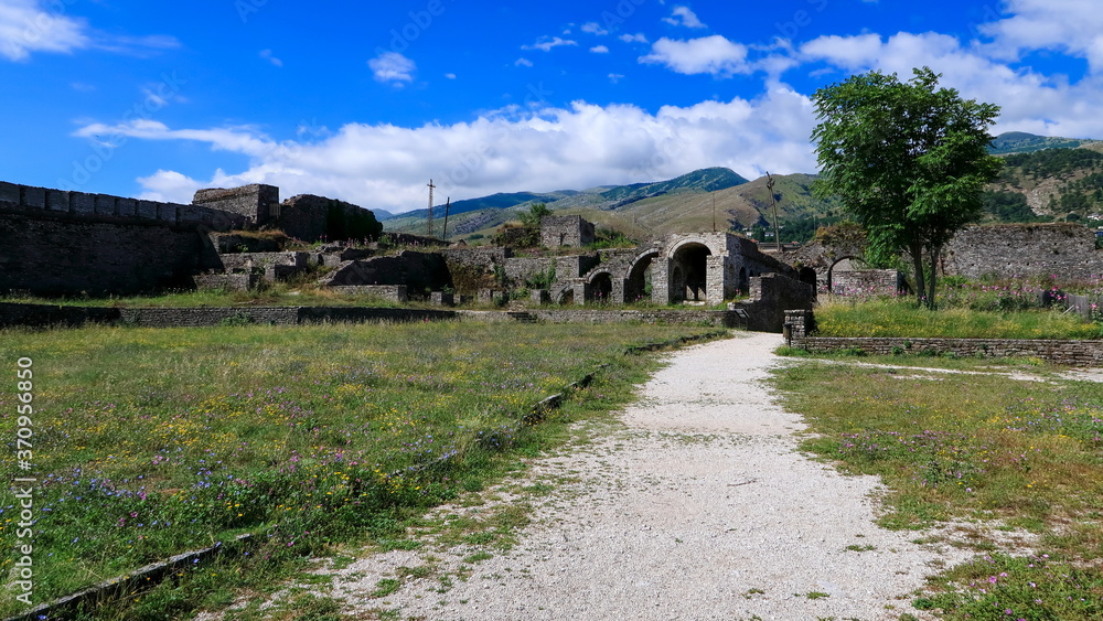 Path leading towards stone ruins with green mountains during a sunny weather. Gjirocaster castle, Albania Path leading towards stone ruins with green mountains during a sunny weather. Gjirocaster castle, Albania