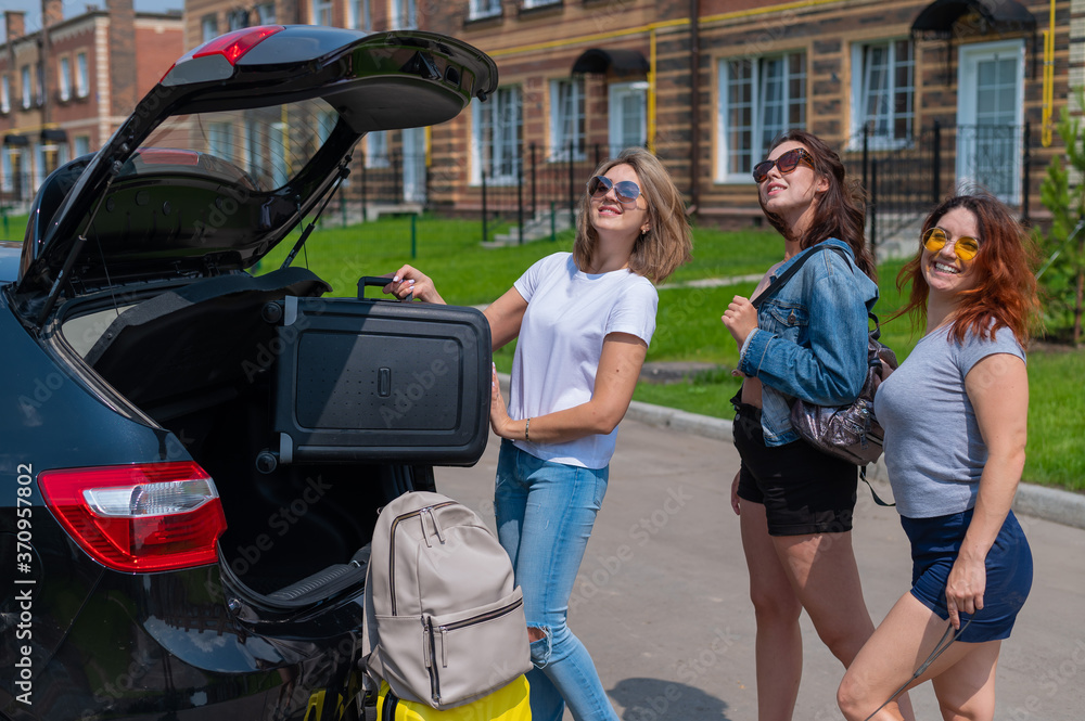 Three friends go on a road trip and load their suitcases into the trunk of the car.