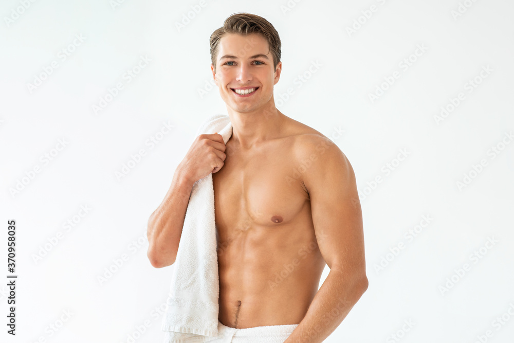 Handsome young man standing with towel at white studio