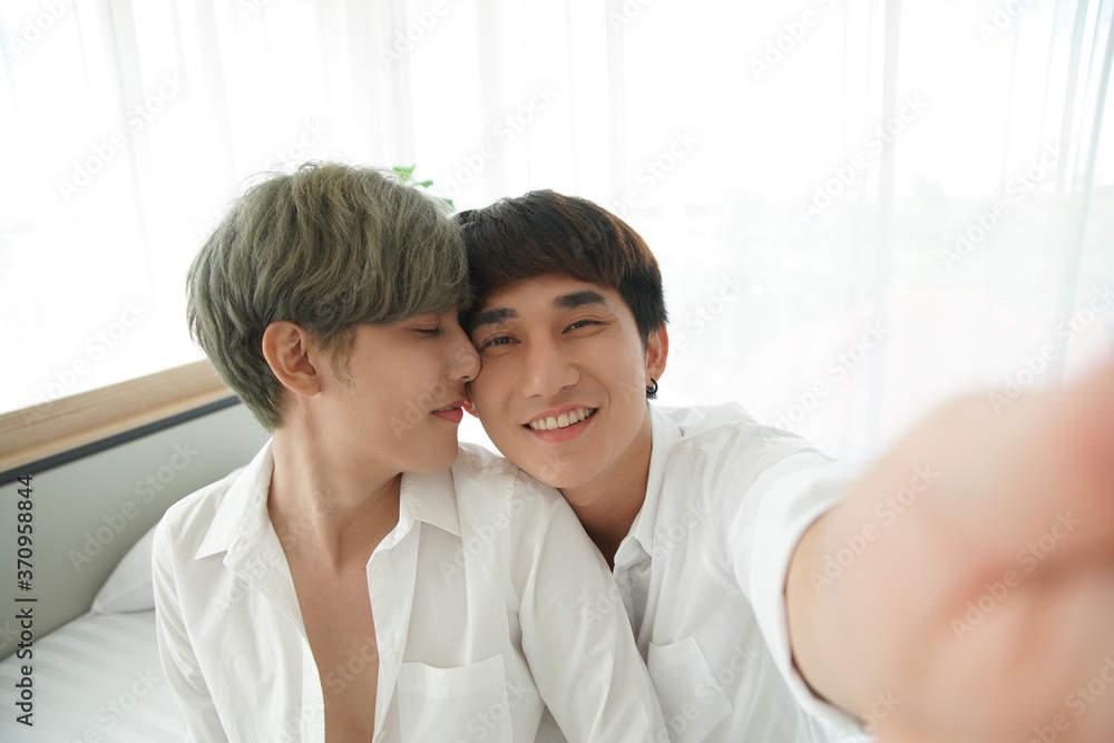LGBT Asian young gay couple kissing while taking a romantic selfie photo together at bedroom LGBT Asian young gay couple kissing while taking a romantic selfie photo together at bedroom