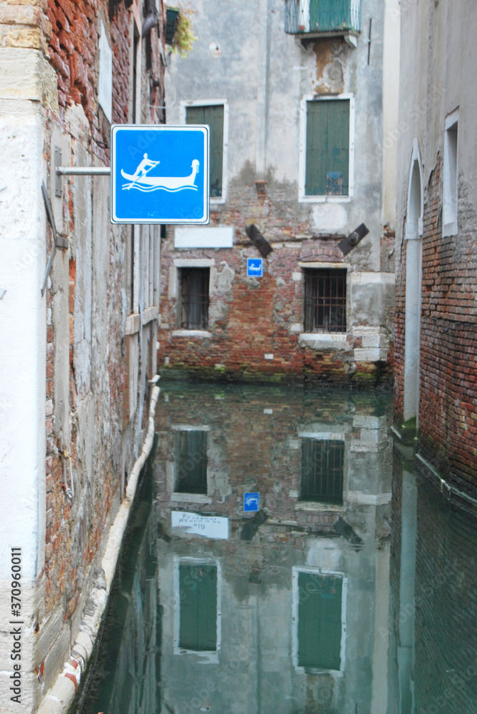 
narrow internal canal in Venice with signs indicating the passage reserved for rowing boats