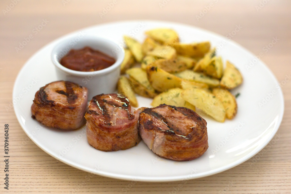 Pork medallions with fried potatoes and ketchup on white plate Pork medallions with fried potatoes and ketchup on white plate