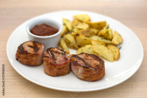 Pork medallions with fried potatoes and ketchup on white plate