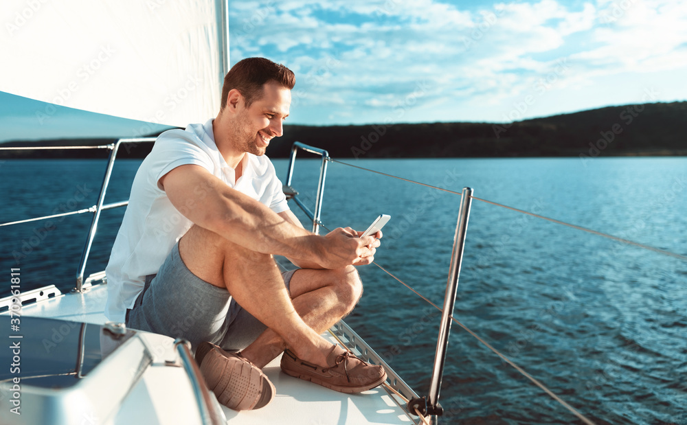 Man Using Smartphone Sitting On Deck Sailing Across Sea Outdoors