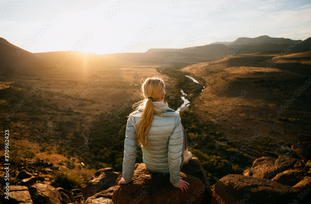 Caucasian female sitting on a rock on top of a mountain enjoying sunset after a hike, amazing view