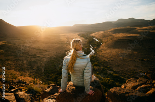 Caucasian female sitting on a rock on top of a mountain enjoying sunset after a hike, amazing view