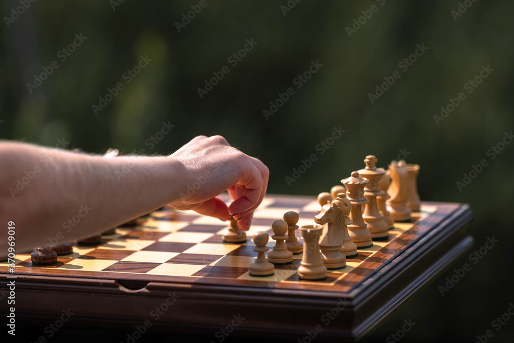 I am playing chess alone. Female hand moves pawn on chessboard with set pieces. Wooden