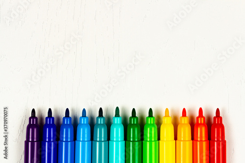 bright colored markers without caps lie on a white wooden table