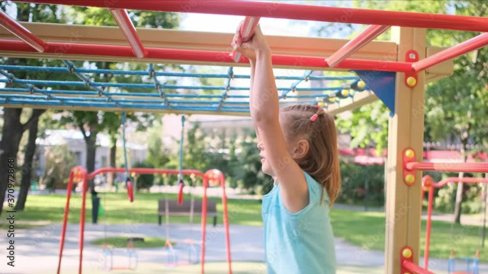 Little girl hanging on monkey bars in park on playground Little girl hanging on monkey bars in park on playground