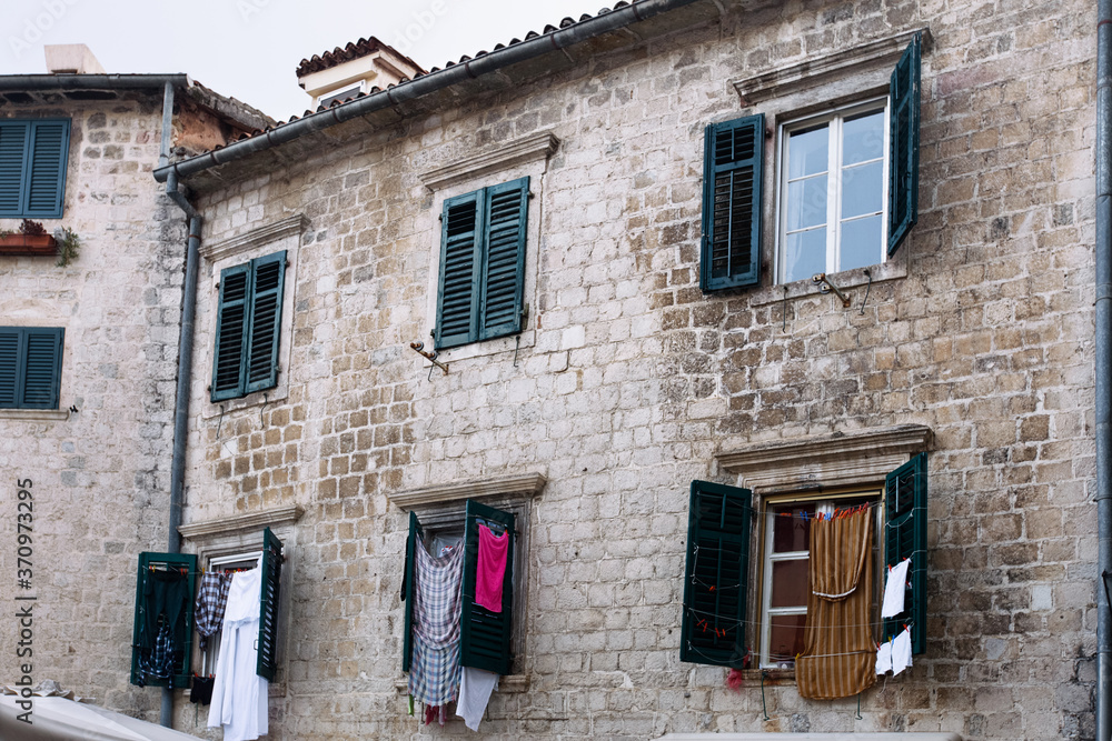 Medieval brick building facade windows with closed and opened wood shutters and drying laundry on it. Montenegro, Kotor.