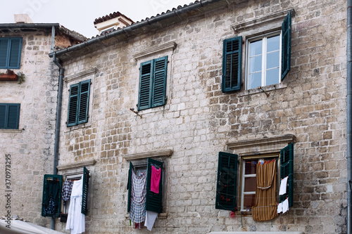 Obraz na płótnie Medieval brick building facade windows with closed and opened wood shutters and drying laundry on it. Montenegro, Kotor. w salonie