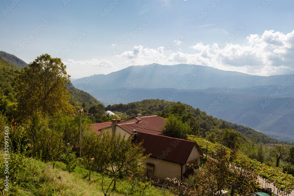 Little farm house with farmstead on th slops. Far mountains and white clouds background. Montenegro. Rural mountain landscape.