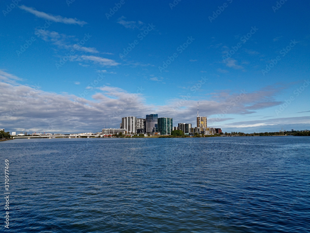 Naklejka premium Beautiful view of high-rise buildings on the riverbank on a sunny day with deep blue sky and light clouds, Parramatta river, Meadowbank, Sydney, New South Wales, Australia 