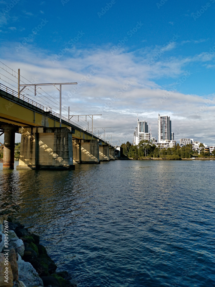Beautiful view of a railway bridge across a river on a sunny day with deep blue sky and light clouds, Parramatta river, Meadowbank, Sydney, New South Wales, Australia
