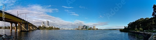 Beautiful view of a railway bridge across a river and high-rise buildings on the riverbank on a sunny day with deep blue sky and light clouds, Parramatta river, Meadowbank, Sydney, New South Wales, Au © Ivan