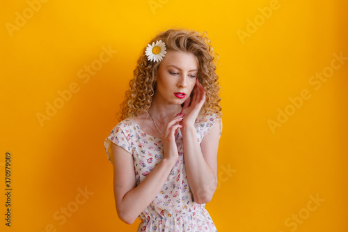Young woman with make-up, curly hair and a Daisy in her hair, isolated on orange background