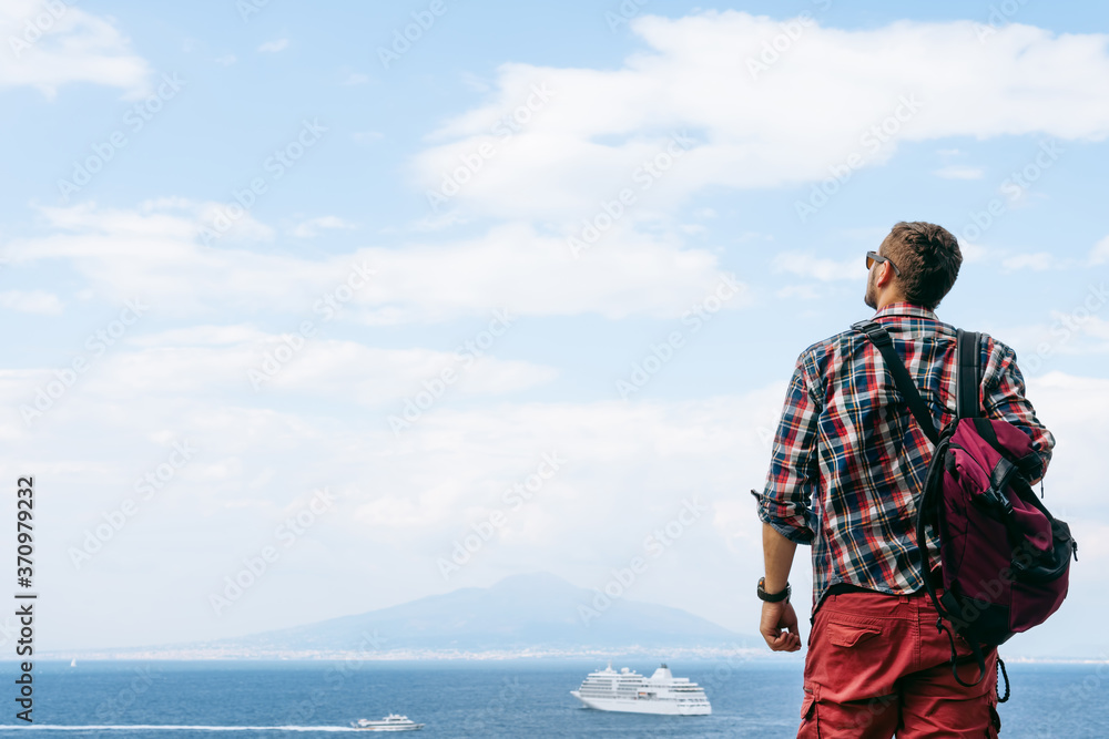 Young man with backpack standing with view on vulcano Vesuvius sea, ocean liner ship water craft. Travel and vacation concept. Copy space