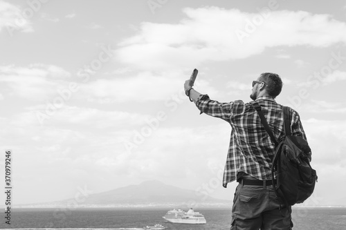 Wallpaper Mural Male tourist with glasses and a banana bag Takes a selfie photo, uses a smartphone. Communication and mobile internet concept. Roaming View of the sea and Mount Vesuvius. Ocean liner. Black and white Torontodigital.ca