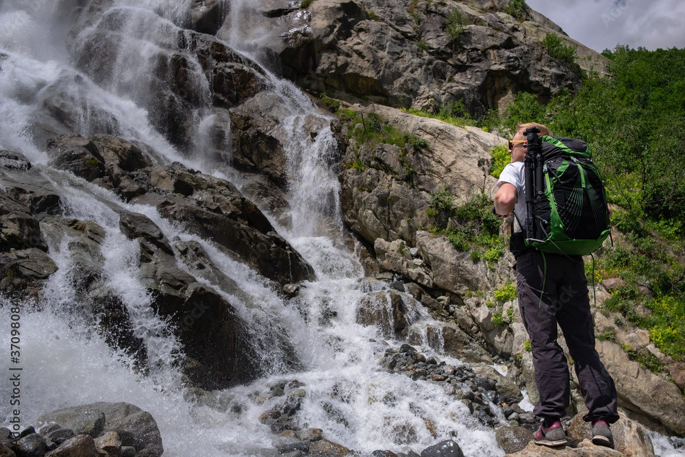 Obraz premium Man hiking with backpack looking at waterfall. Portrait of male adult back standing outdoor.