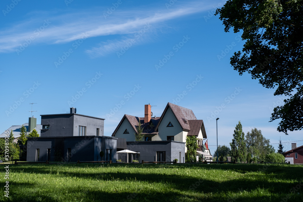 two residential houses on the outskirts of a small town in the middle of summer when everything is surrounded by green grass and green trees