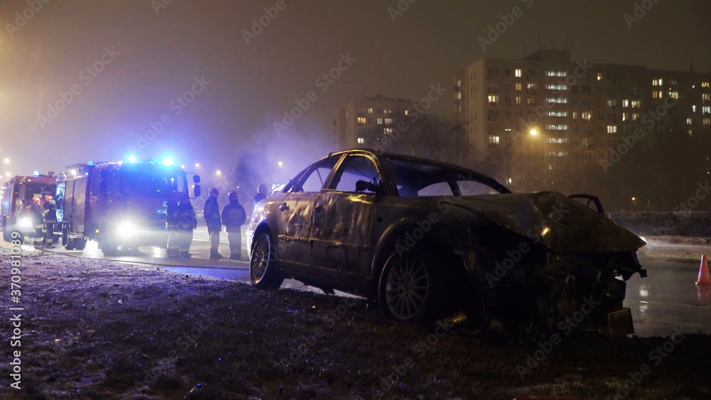 Winter car accident, burned car with fire engine and buildings in the background. High quality photo
