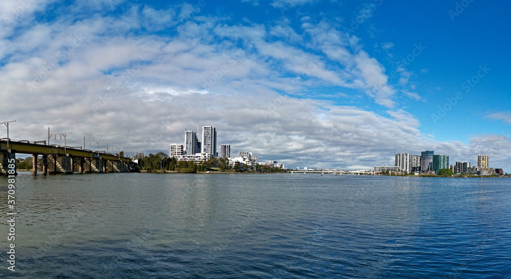 Beautiful panoramic view of high-rise buildings on the riverbank on a sunny day with deep blue sky and light clouds, Parramatta river, Meadowbank, Sydney, New South Wales, Australia

