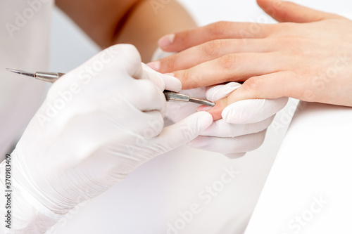 Fototapeta Naklejka Na Ścianę i Meble -  Hands of manicurist pushing cuticles on female's nails with manicure tool. Woman receiving manicure and nail care procedure