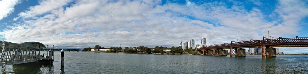Beautiful panoramic view of a wharf and a railway bridge across a river on a sunny day with deep blue sky, Parramatta river, Meadowbank, Sydney, New South Wales, Australia
